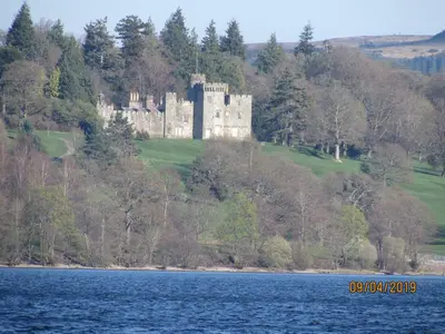 a castle on a hill next to a body of water at Levenhowe Holiday Apartment in Balloch