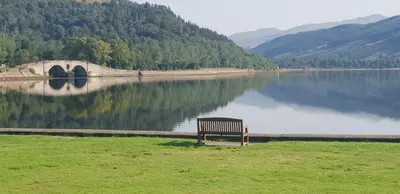 a bench sitting on the grass near a body of water at CREAG DHUBH COUNTRY HOUSE in Inveraray