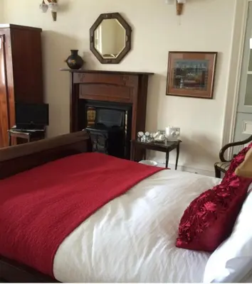 a bedroom with a bed with a red blanket and a mirror at Hunters Guest House in Brodick