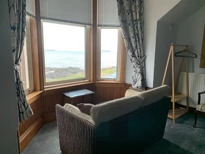 a living room with a couch and two windows at Hunters Guest House in Brodick