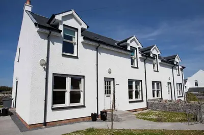 a white house with black windows and a stone wall at Killinallan Cottage in Port Charlotte