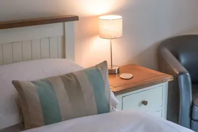 a bedroom with a bed with a lamp and a chair at Killinallan Cottage in Port Charlotte