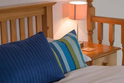 a bed with a blue pillow and a table with a lamp at Ardnave in Port Charlotte