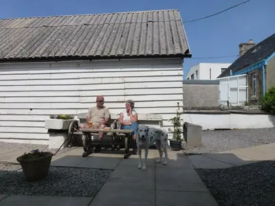 a man and a woman sitting on a bench with a dog at Argyll Hotel in Bellochantuy