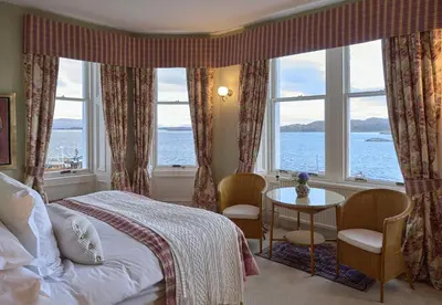 a bedroom with a bed and a table and windows at Crinan Hotel in Crinan