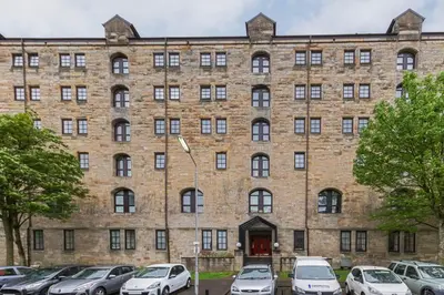 a large brick building with cars parked in a parking lot at Stunning 2 Bed Merchant City Apartment with Residents Parking (Bell 2) in Glasgow