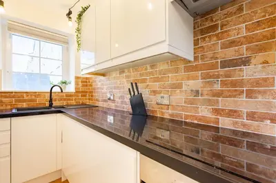a kitchen with white cabinets and a brick wall at Central, Bright 2 Bed Flat - Pool & Sauna in Edinburgh