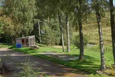 a park with a bench in the grass with trees at Cosy Rowan woodland lodge no3 in Killin