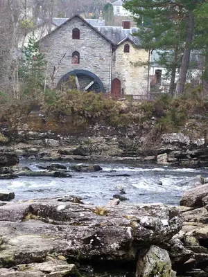 an old stone building sitting next to a river at Cosy Rowan woodland lodge no3 in Killin