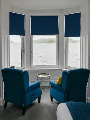 two blue chairs and a table in a room with windows at MacKays in Oban