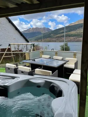 a hot tub on a patio with a view of a lake at Amazing Alps and Loch views - HOT TUB and pet friendly in Arrochar