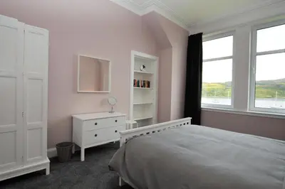 a white bedroom with a bed and a window at Upper Alta Apartment in Tighnabruaich