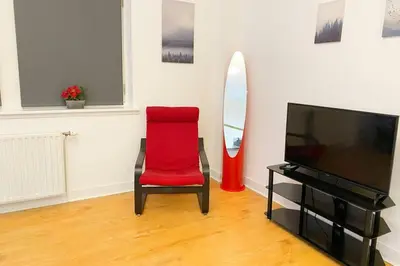 a red chair in a living room with a television at Cozy Nights - Ibrox Street in Glasgow