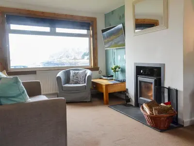 a living room with a fireplace and a chair at Seaview Cottage in Ellanbeich