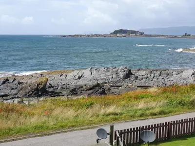 a road with a view of the ocean and a beach at Seaview Cottage in Ellanbeich
