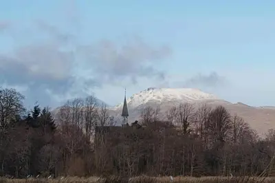 a snow covered mountain with a church and a church tower at Broomfield Cottage South Luss in Glasgow