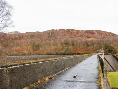 a bridge over a river next to a mountain at Glenfinglas Dam Cottage in Callander