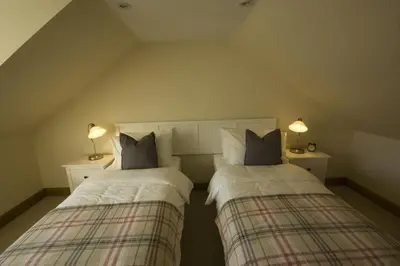 two beds in a room with two lamps on tables at Harviestoun House in Dollar