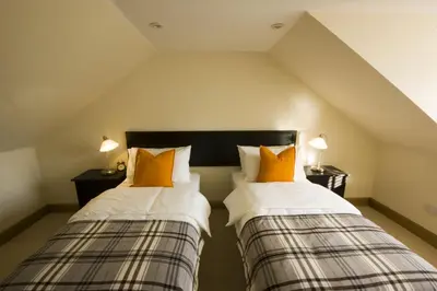 two beds with orange pillows in a attic room at Harviestoun House in Dollar