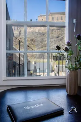 a book on a table with a vase of flowers and a window at Castle Vista, Grassmarket Apartment in Edinburgh
