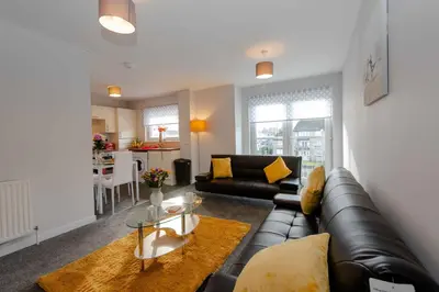 a living room with a black leather couch and a table at PREMIER - Wishaw En-Suite Apartment in Wishaw