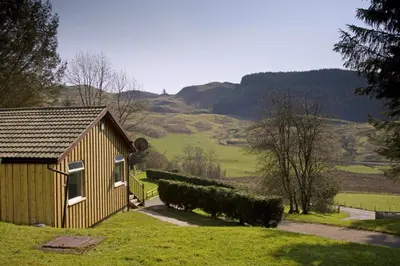 a small house in a field with mountains in the background at Lagnakeil Highland Lodges in Oban