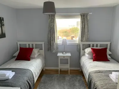 two beds with red pillows in a room with a window at Flat One, 212 Eaglesham Road, East Kilbride, Glasgow in Glasgow