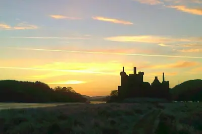 a silhouette of a building in a field at sunset at Fern Lodge in Dalavich