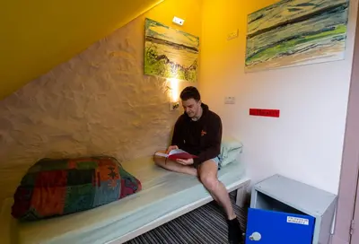 a man sitting on a bed reading a book at Castle Rock Hostel - Adults Only in Edinburgh