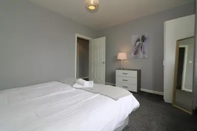 a bedroom with a white bed and a dresser and a mirror at Signature - Carfin House in Carfin