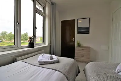 a bedroom with two beds and two windows at Signature - Carfin House in Carfin