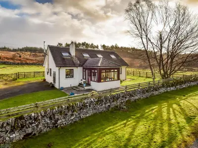 a small white house with a stone wall at Borgan Cottage in Newton Stewart