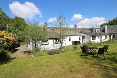 a white house with a table and chairs in a yard at Ben Lomond Cottage in Gartocharn
