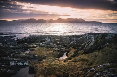 a sunset over the ocean with rocks and water at Auchnabreac Cottage in Carradale