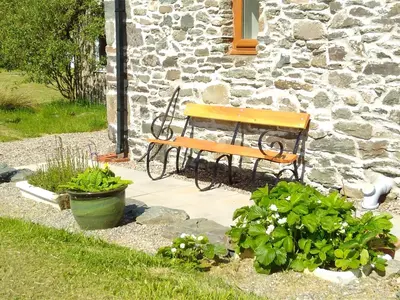 a wooden bench sitting in front of a stone building at Auchnabreac Cottage in Carradale
