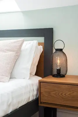 a lamp on a wooden table next to a bed at City Centre, Newly Refurbished Stylish Apartment in Edinburgh