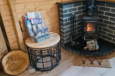 a room with a fireplace and a table with a wood stove at 1-Bed Cabin 2 adults Wood Burning Hot Tub & Fire in Carluke