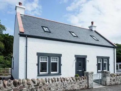 a white house with a stone wall at Squirrel Cottage in Stranraer