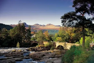 a bridge over a river with mountains in the background at Woodland Hazel Lodge in Killin