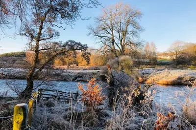 a snow covered field with a river and trees at Barns Bothy in Peebles