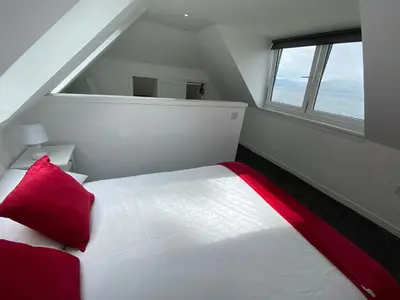 a bedroom with a white bed with a red pillow at The Wee Cottage by the Ferry in Gourock