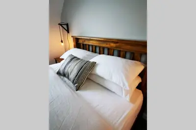 a bed with white pillows and a wooden headboard at 2 Calgow Cottages in Newton Stewart