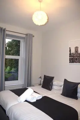 two beds in a bedroom with a window and a chandelier at Kelpies Serviced Apartments- Victoria in Falkirk