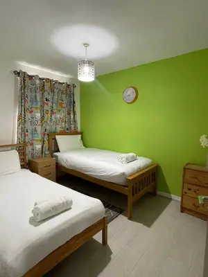 a green room with two beds and a clock on the wall at Chic 2 Bed Apartment with Free Parking- Recently Redecorated, 10 Minutes to City Centre in Edinburgh