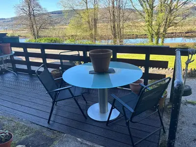 a table and chairs on a deck with a cup on it at North Lodge Kilmun in Kilmun