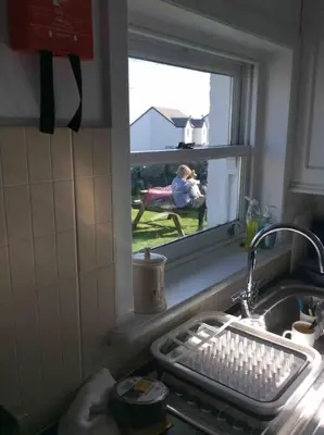 a kitchen sink with a window with a woman sitting in a chair at Upper Imeraval Cottage Sleeps 6 Pet-Friendly in Port Ellen