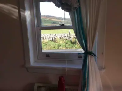 a window with a curtain with a view of a field at Upper Imeraval Cottage Sleeps 6 Pet-Friendly in Port Ellen