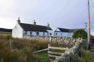 a stone fence in front of a white house at Upper Imeraval Cottage Sleeps 6 Pet-Friendly in Port Ellen