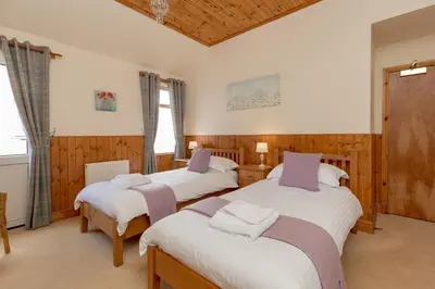 two twin beds in a room with wooden walls at Doonans Cottage in Maybole