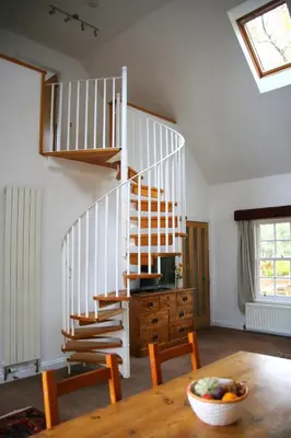 a dining room with a table and a spiral staircase at Pirn Mill Self Catering Cottage in Cladich